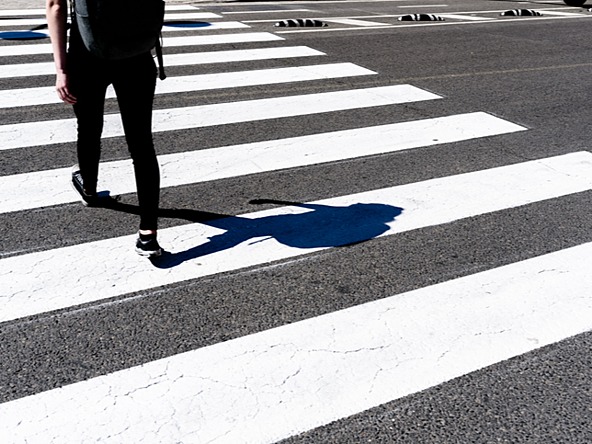 back of person walking over pedestrian crossing, with shadow on ground